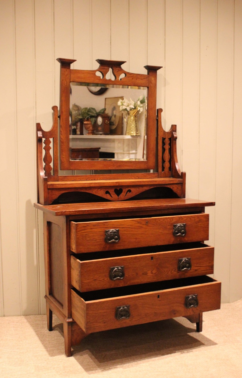 A solid oak Arts and Crafts dressing chest featuring three wide drawers, metal drop handles, heart-shaped cutouts, and a tilting rectangular mirror on top. View VIII