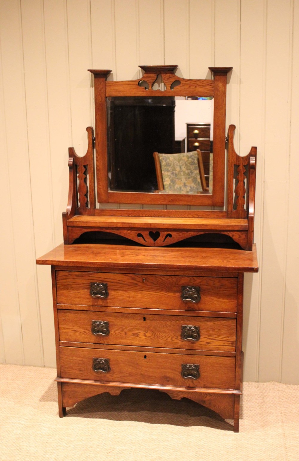 A solid oak Arts and Crafts dressing chest featuring three wide drawers, metal drop handles, heart-shaped cutouts, and a tilting rectangular mirror on top. View IX