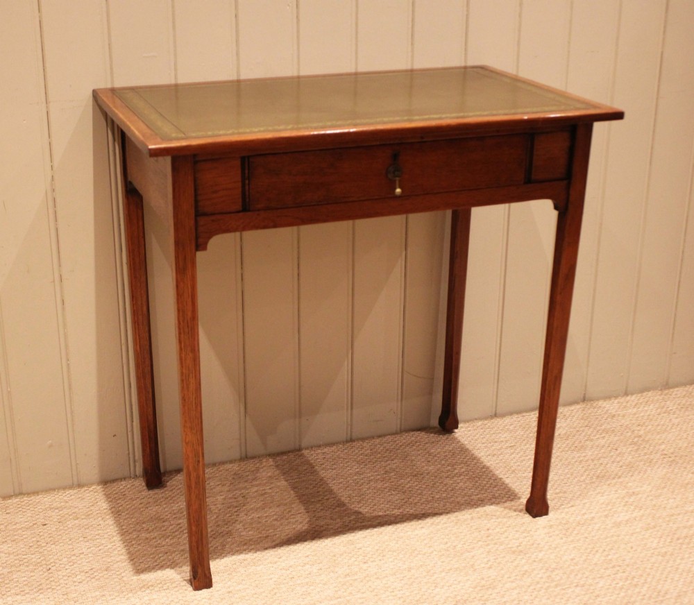A small rectangular Arts and Crafts oak writing desk with a green gilded leather inset top, a single frieze drawer, and tapered square legs. View II