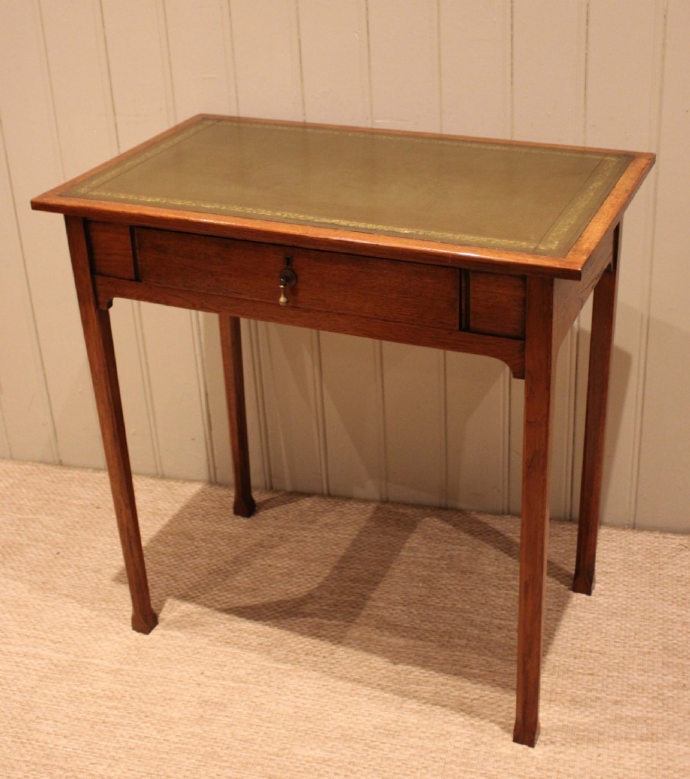 A small rectangular Arts and Crafts oak writing desk with a green gilded leather inset top, a single frieze drawer, and tapered square legs. View IV