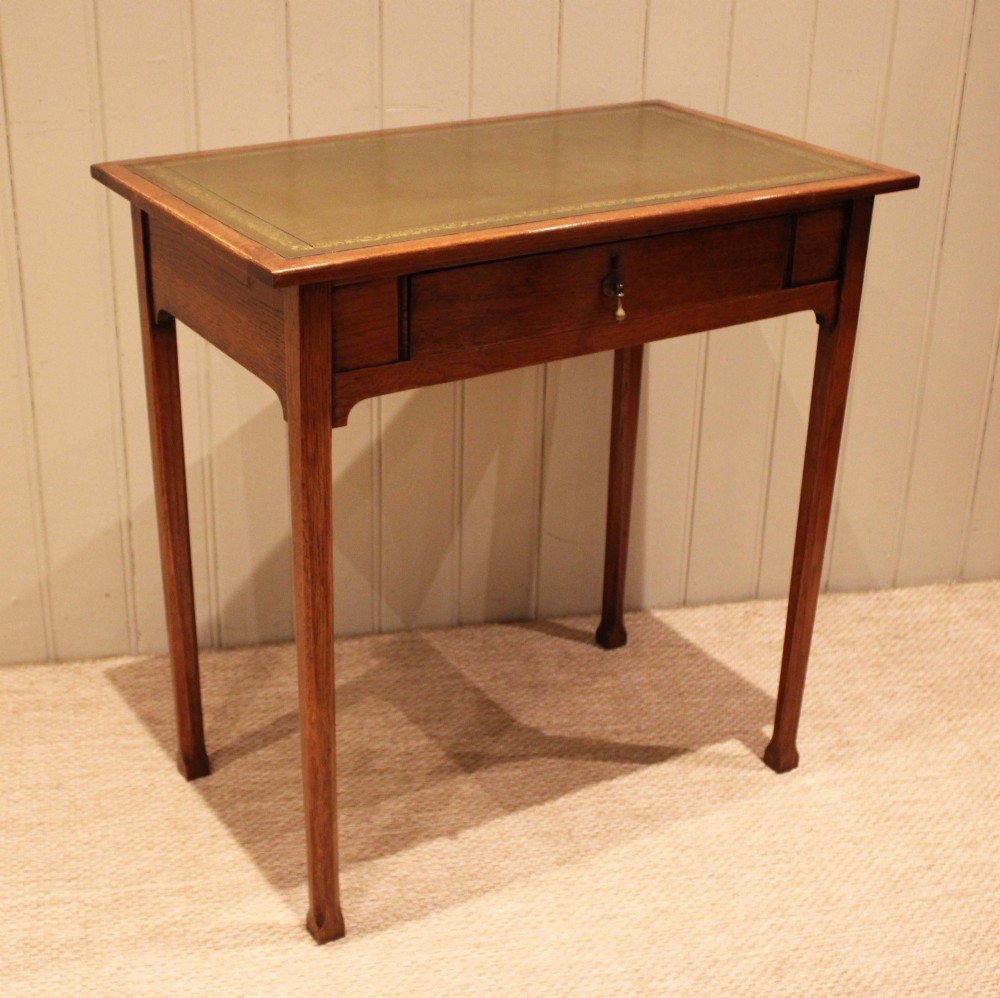 A small rectangular Arts and Crafts oak writing desk with a green gilded leather inset top, a single frieze drawer, and tapered square legs. View V