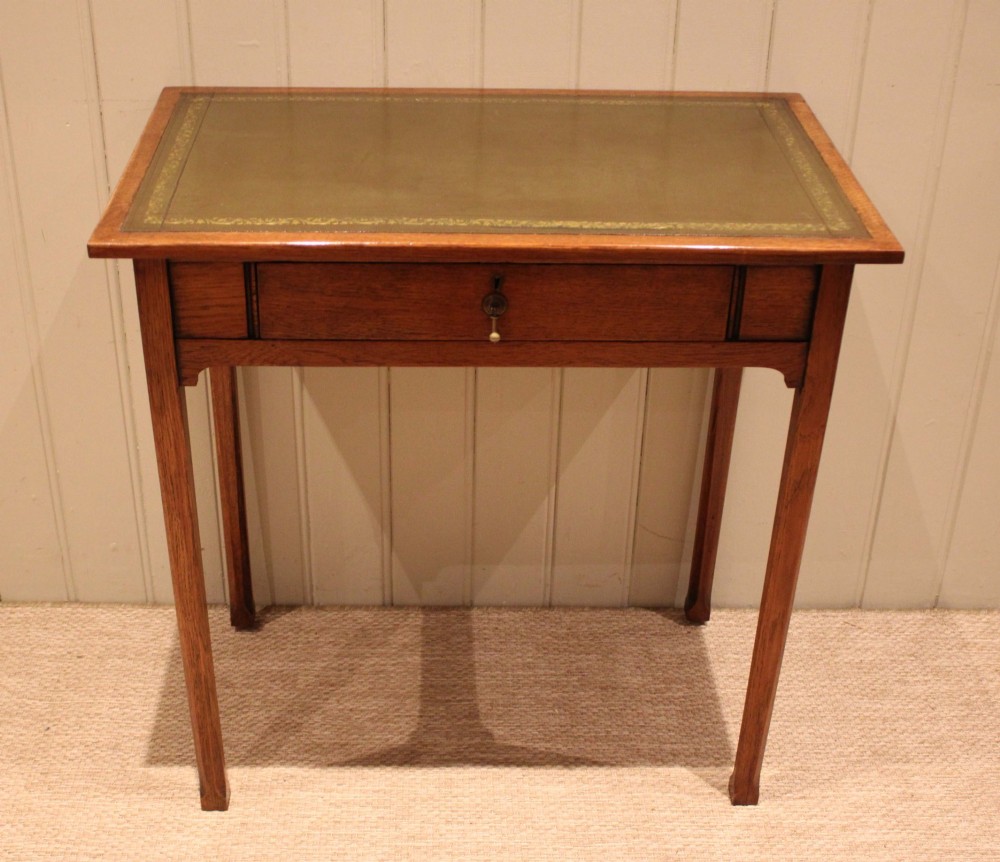 A small rectangular Arts and Crafts oak writing desk with a green gilded leather inset top, a single frieze drawer, and tapered square legs. View VI