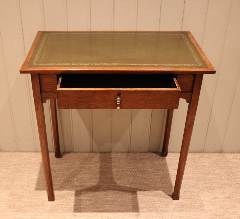 A small rectangular Arts and Crafts oak writing desk with a green gilded leather inset top, a single frieze drawer, and tapered square legs. View VIII