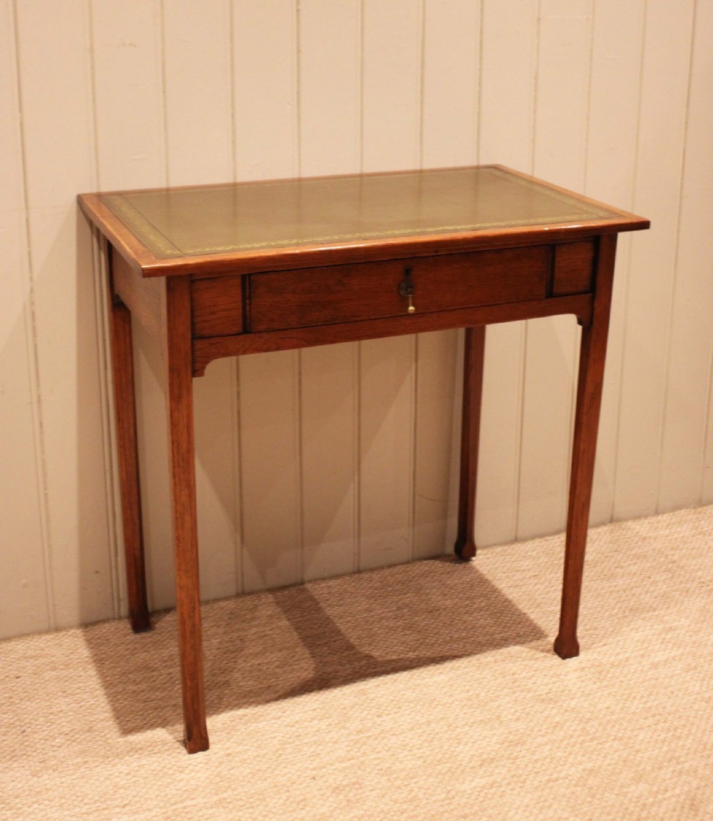 A small rectangular Arts and Crafts oak writing desk with a green gilded leather inset top, a single frieze drawer, and tapered square legs. View IX