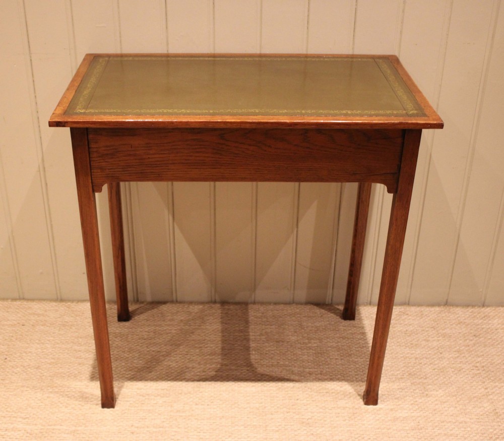 A small rectangular Arts and Crafts oak writing desk with a green gilded leather inset top, a single frieze drawer, and tapered square legs. View XI