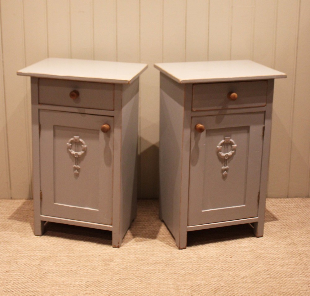 A pair of light grey painted pine bedside cabinets, each featuring a single upper drawer above a cupboard door decorated with a carved wreath motif. View II