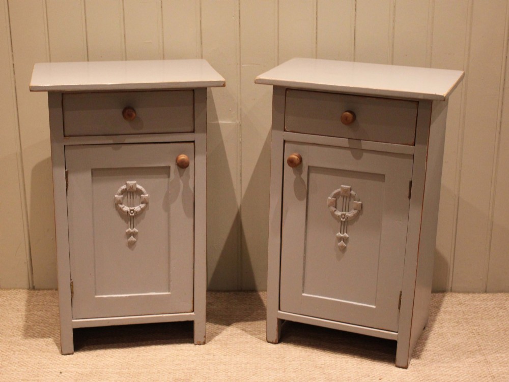 A pair of light grey painted pine bedside cabinets, each featuring a single upper drawer above a cupboard door decorated with a carved wreath motif. View VI