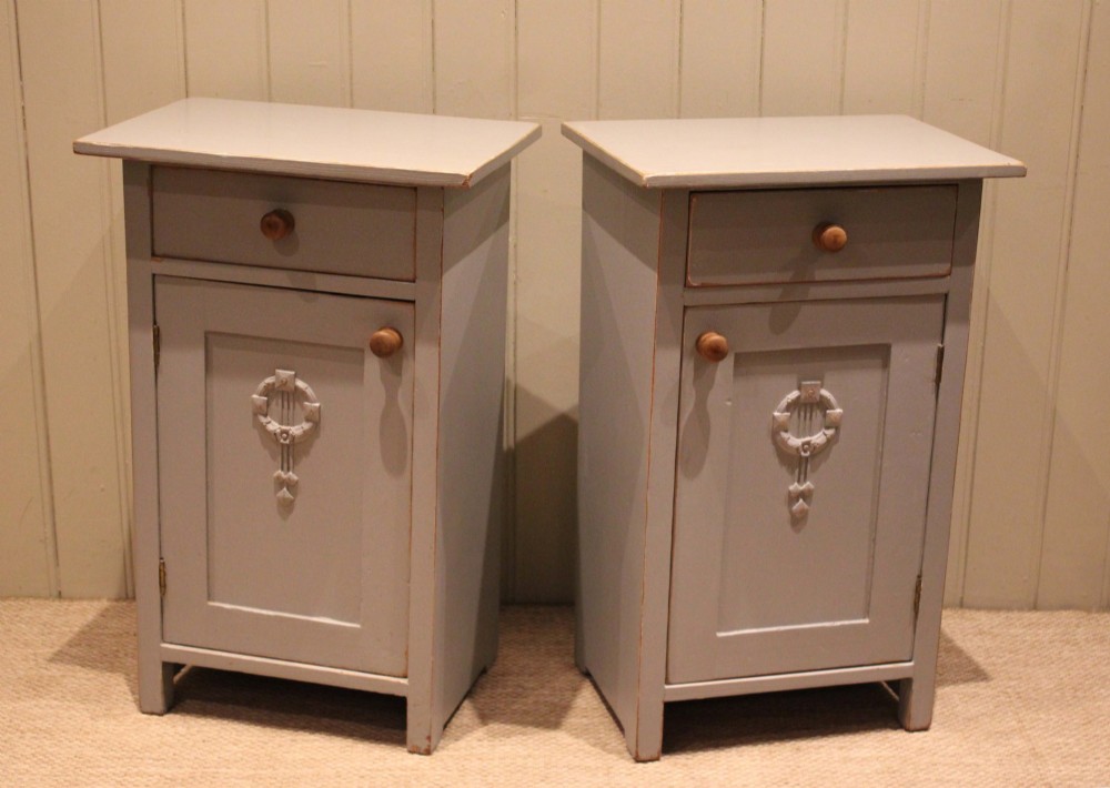 A pair of light grey painted pine bedside cabinets, each featuring a single upper drawer above a cupboard door decorated with a carved wreath motif. View VII