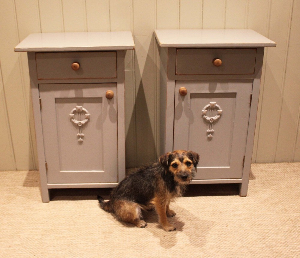 A pair of light grey painted pine bedside cabinets, each featuring a single upper drawer above a cupboard door decorated with a carved wreath motif. View VIII