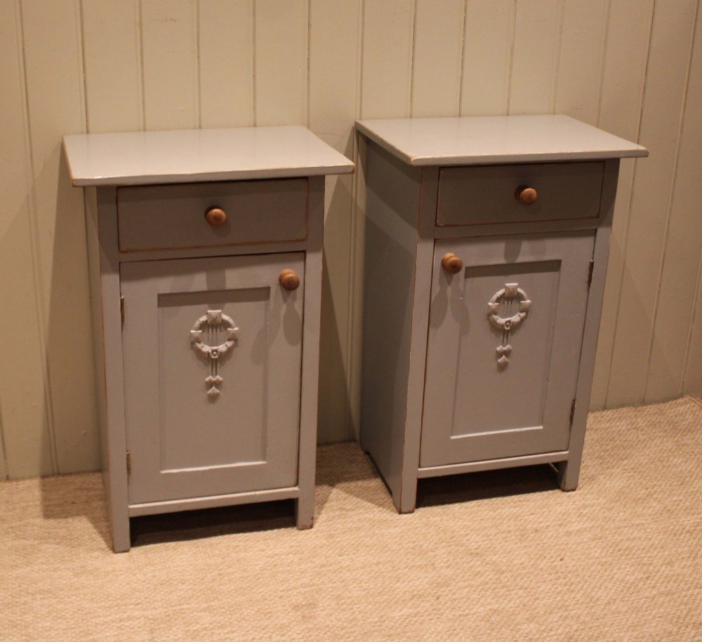 A pair of light grey painted pine bedside cabinets, each featuring a single upper drawer above a cupboard door decorated with a carved wreath motif. View IX