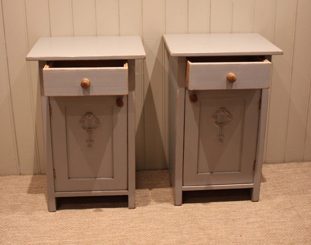A pair of light grey painted pine bedside cabinets, each featuring a single upper drawer above a cupboard door decorated with a carved wreath motif. View X