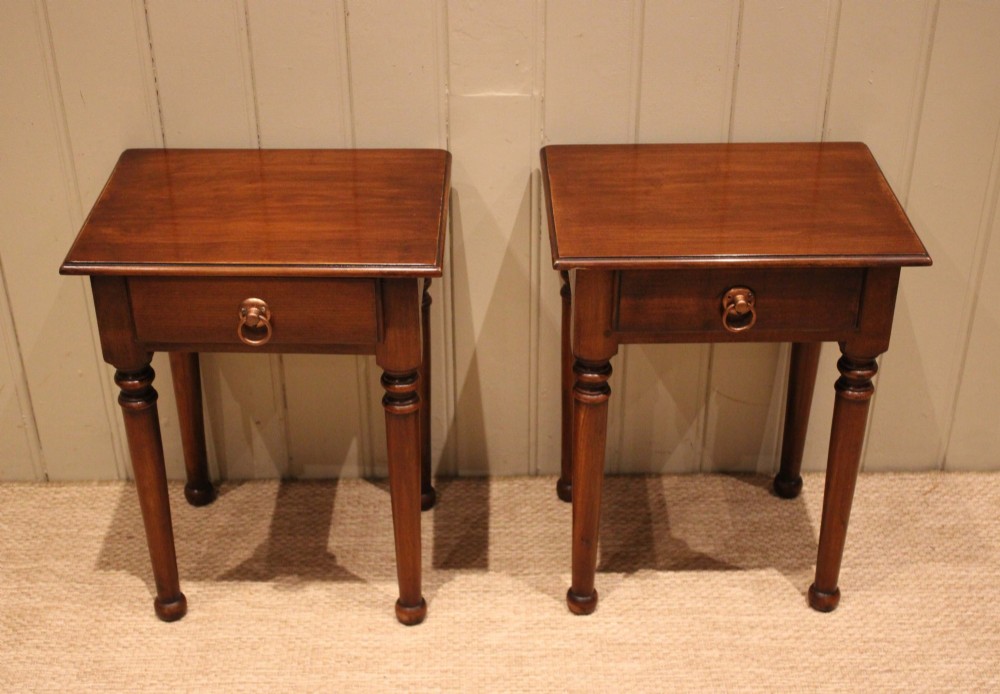 A pair of warm brown French cherry wood bedside tables featuring single drawers with brass ring pulls and slender turned legs.