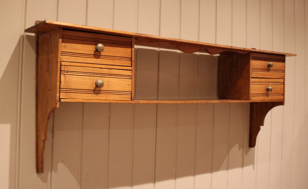 A French poplar wooden wall shelf featuring four side drawers, a central open compartment, and carved lower wall brackets.
