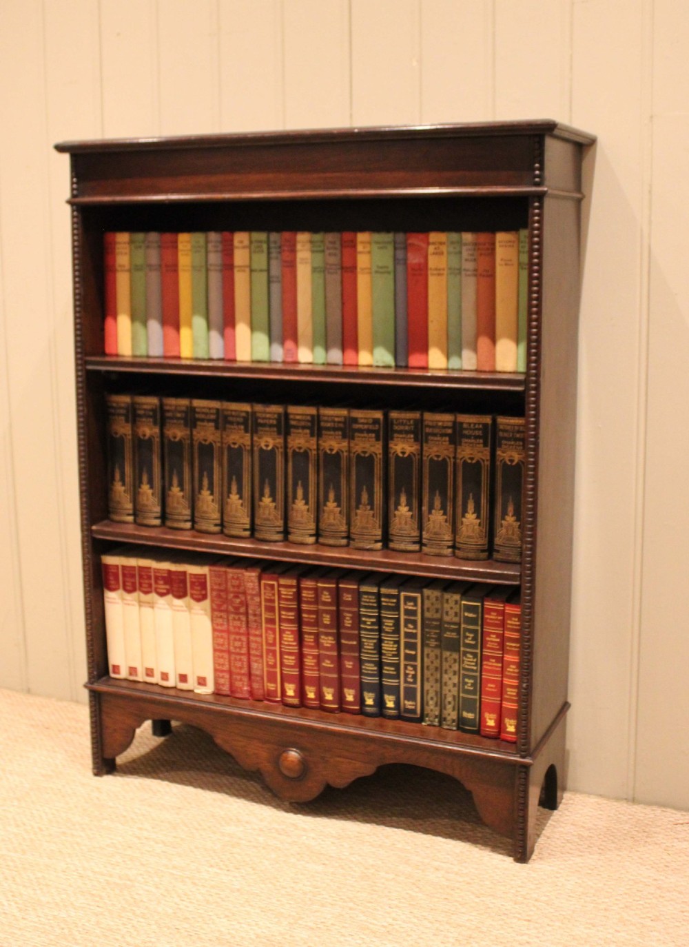 A dark oak open bookcase featuring three adjustable shelves, beaded moulding along the side columns, and a decorative shaped bottom apron with a central circular boss. View III