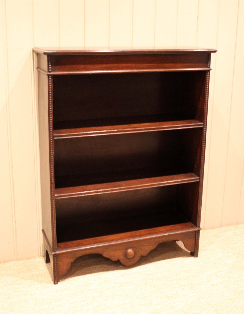 A dark oak open bookcase featuring three adjustable shelves, beaded moulding along the side columns, and a decorative shaped bottom apron with a central circular boss. View IV