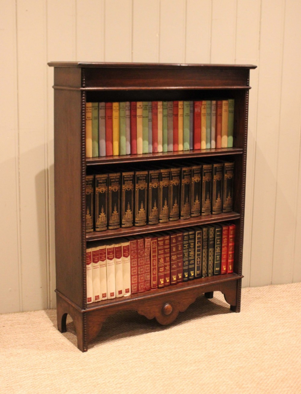 A dark oak open bookcase featuring three adjustable shelves, beaded moulding along the side columns, and a decorative shaped bottom apron with a central circular boss. View VII