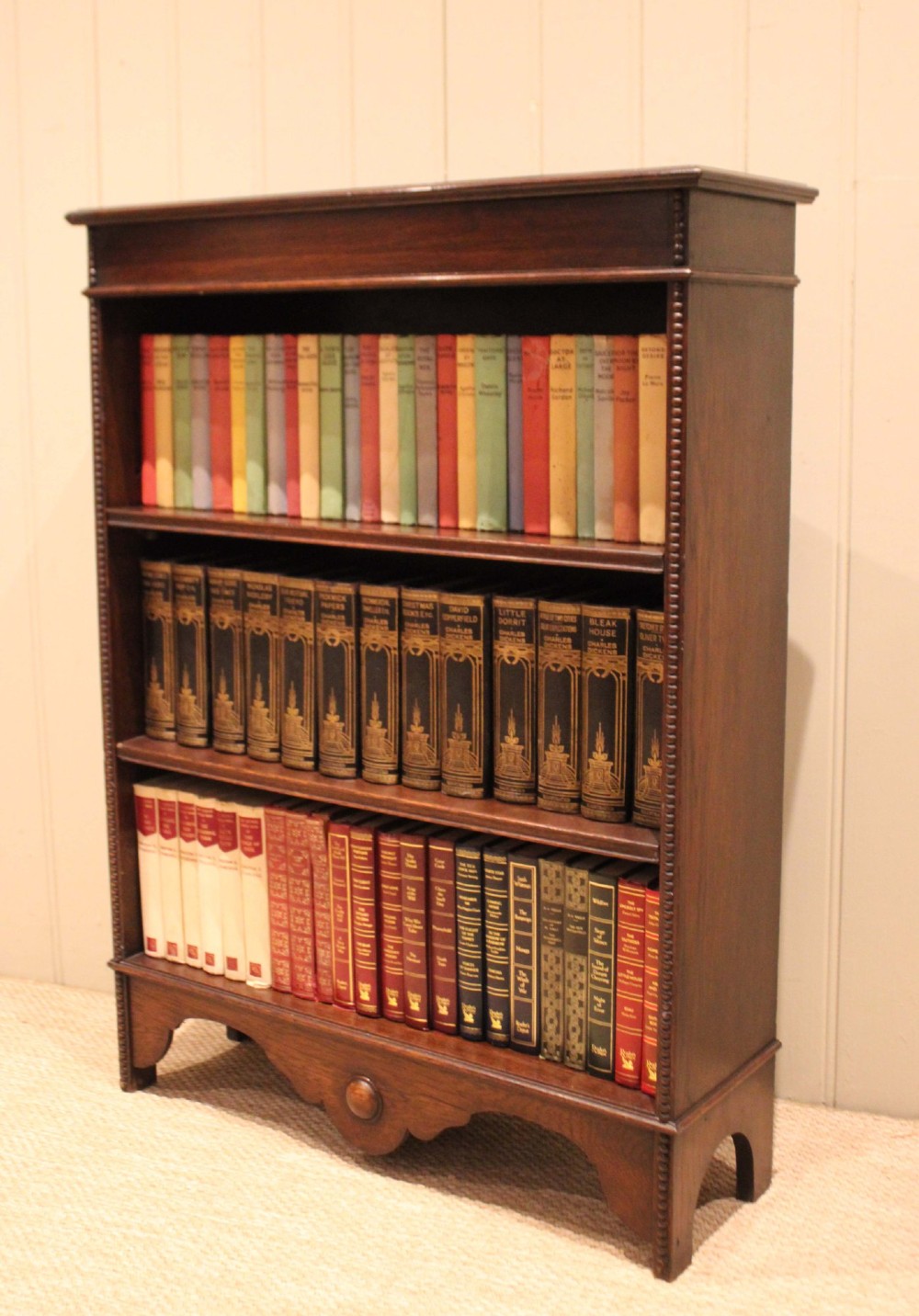 A dark oak open bookcase featuring three adjustable shelves, beaded moulding along the side columns, and a decorative shaped bottom apron with a central circular boss. View IX