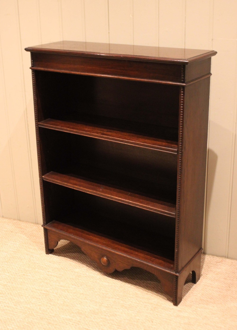 A dark oak open bookcase featuring three adjustable shelves, beaded moulding along the side columns, and a decorative shaped bottom apron with a central circular boss. View XI