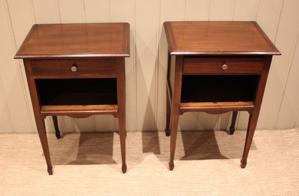 A matching pair of warm brown mahogany bedside tables, each featuring a single top drawer with a central brass knob pull above an open compartment, supported by slender tapered legs.
