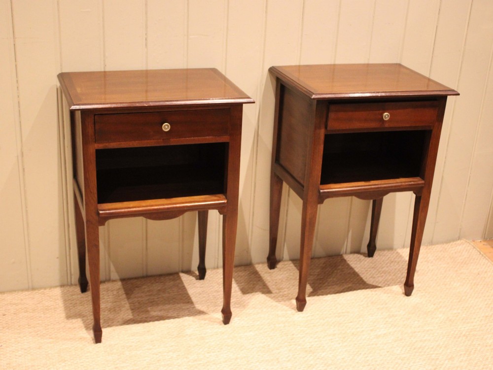 A matching pair of warm brown mahogany bedside tables, each featuring a single top drawer with a central brass knob pull above an open compartment, supported by slender tapered legs. View II