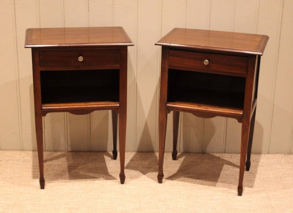 A matching pair of warm brown mahogany bedside tables, each featuring a single top drawer with a central brass knob pull above an open compartment, supported by slender tapered legs. View V