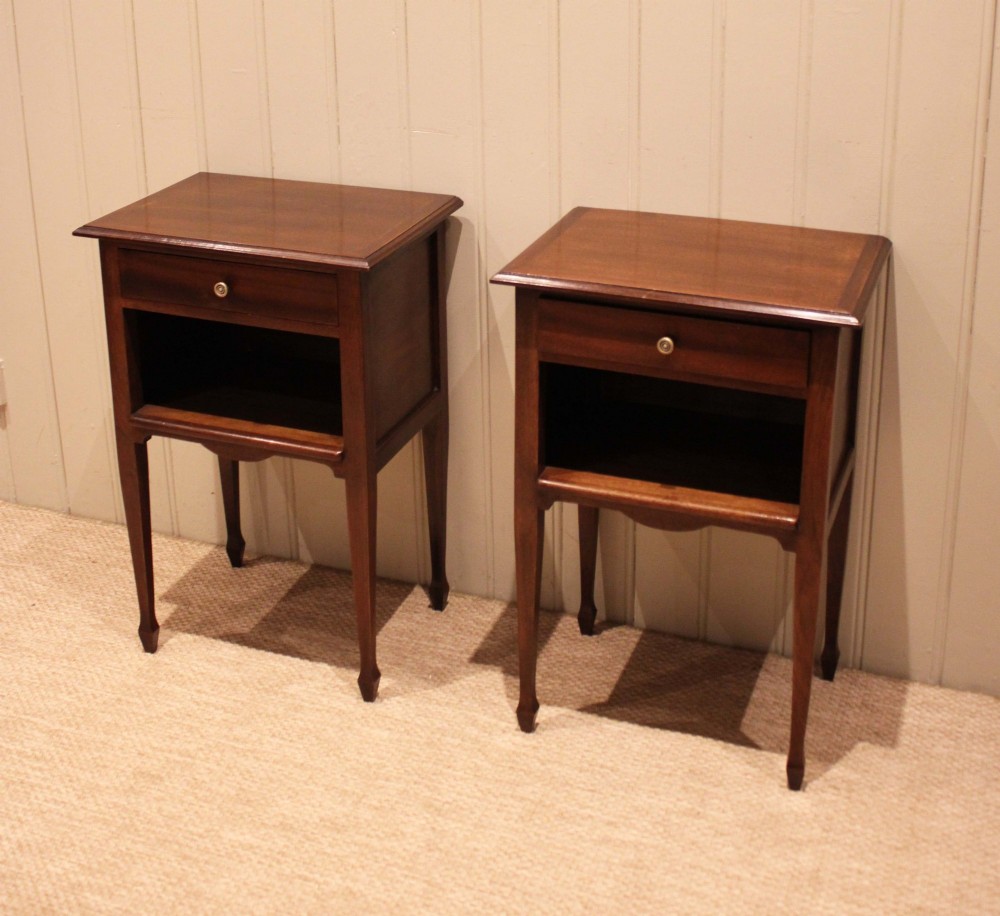 A matching pair of warm brown mahogany bedside tables, each featuring a single top drawer with a central brass knob pull above an open compartment, supported by slender tapered legs. View VII