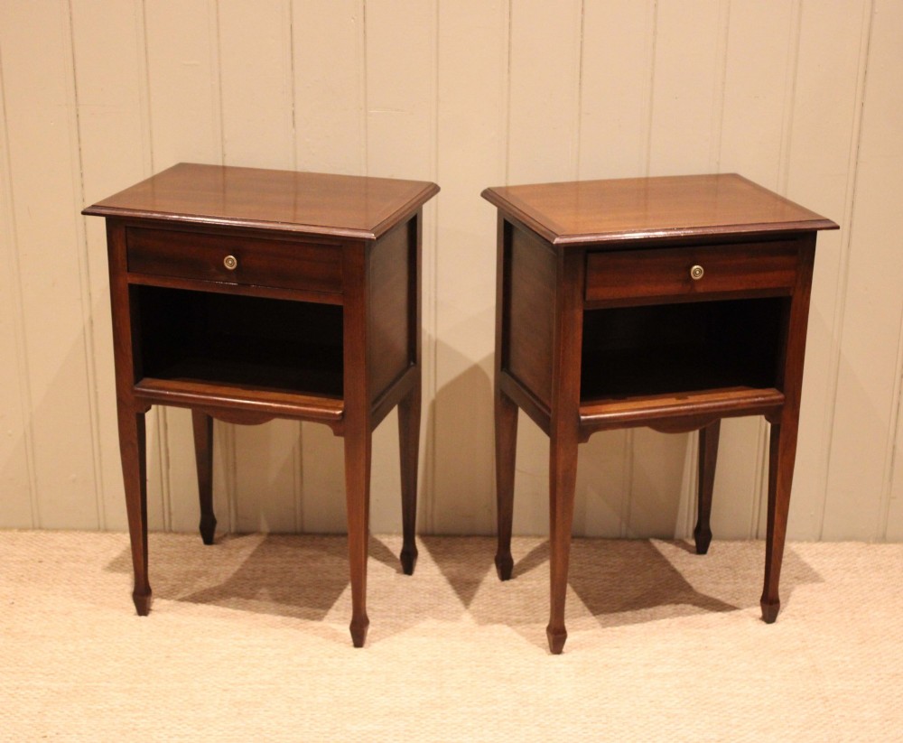 A matching pair of warm brown mahogany bedside tables, each featuring a single top drawer with a central brass knob pull above an open compartment, supported by slender tapered legs. View VIII