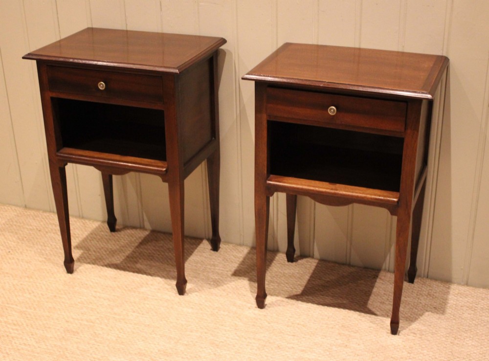 A matching pair of warm brown mahogany bedside tables, each featuring a single top drawer with a central brass knob pull above an open compartment, supported by slender tapered legs. View IX