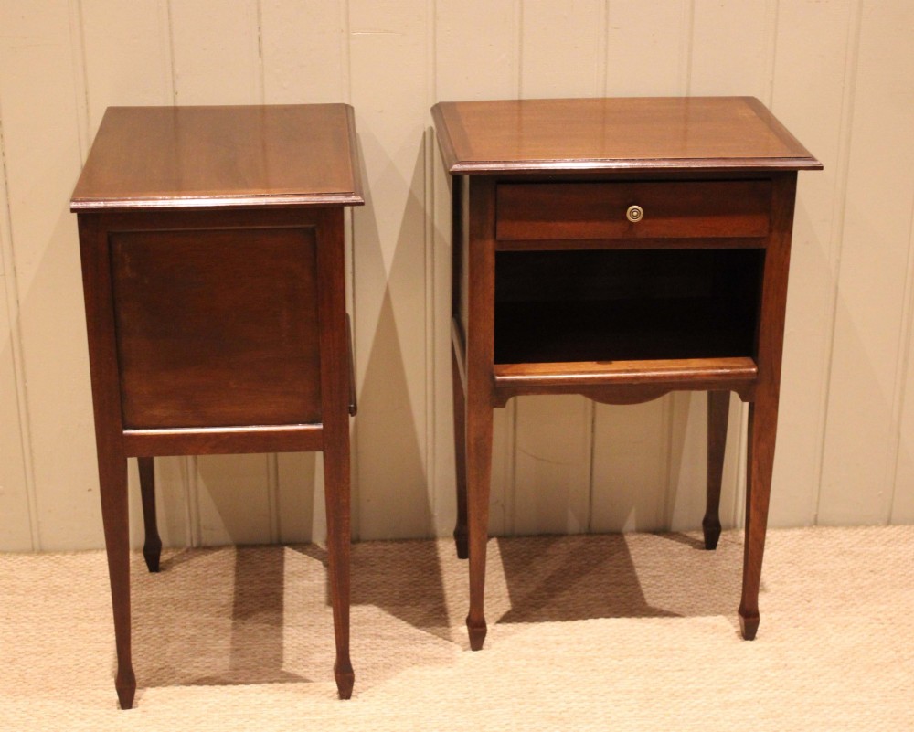 A matching pair of warm brown mahogany bedside tables, each featuring a single top drawer with a central brass knob pull above an open compartment, supported by slender tapered legs. View X