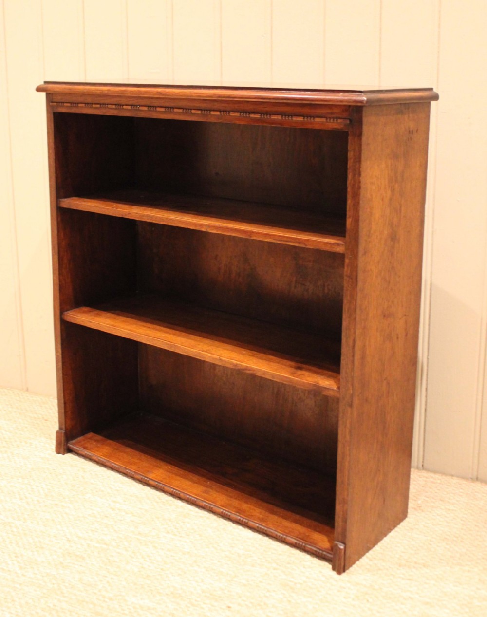 A low open oak bookcase in warm brown featuring three fixed shelves and subtle carved moulding along the top and base edges. View VI