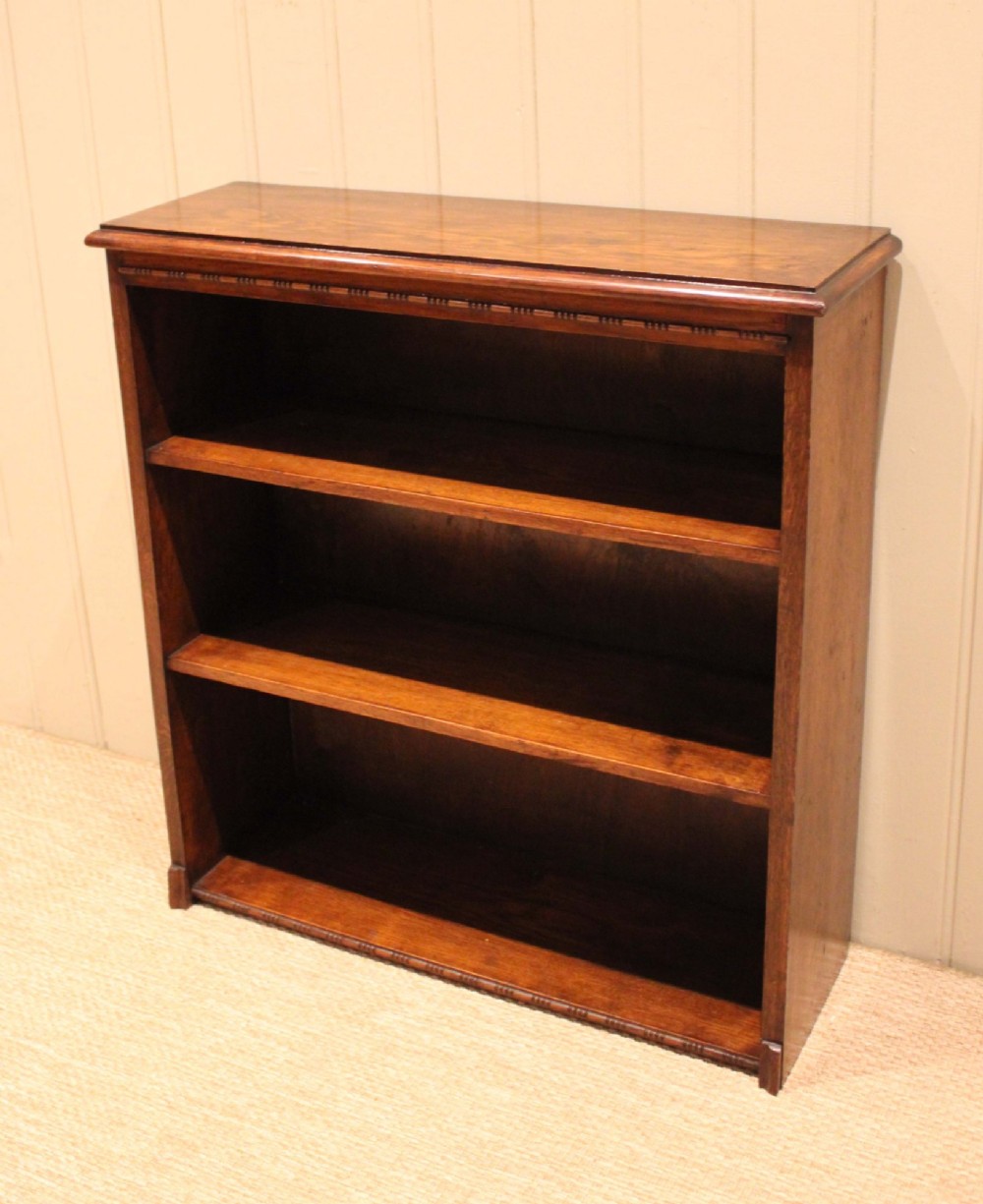 A low open oak bookcase in warm brown featuring three fixed shelves and subtle carved moulding along the top and base edges. View X
