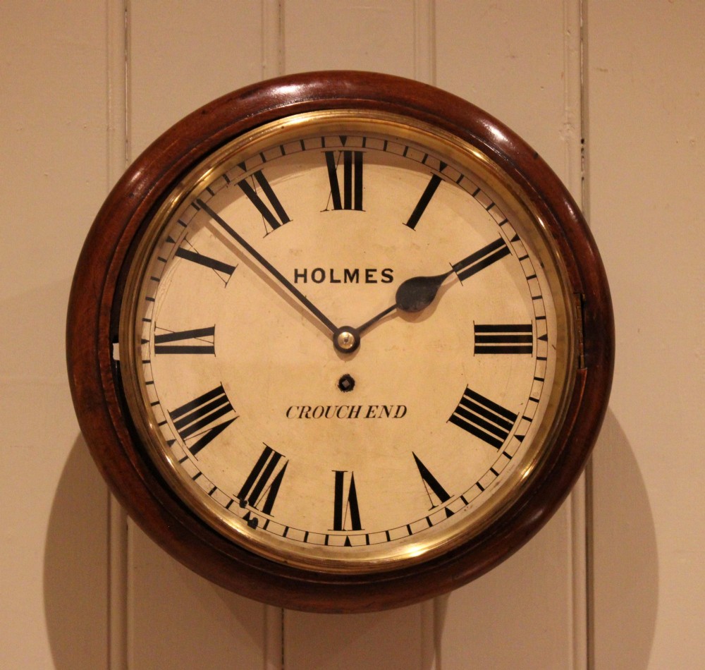 A circular mahogany wall clock featuring a brass bezel surrounding an off-white dial with black Roman numerals.