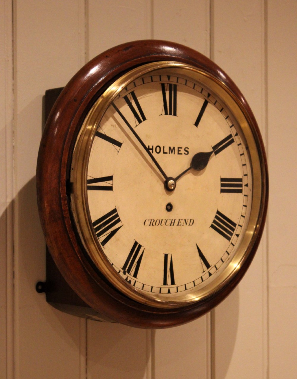 A circular mahogany wall clock featuring a brass bezel surrounding an off-white dial with black Roman numerals. View II