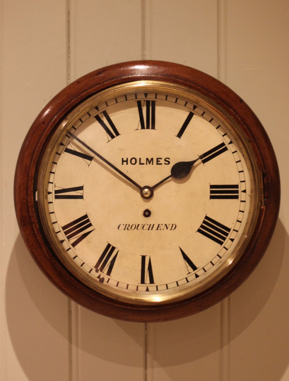 A circular mahogany wall clock featuring a brass bezel surrounding an off-white dial with black Roman numerals. View IV