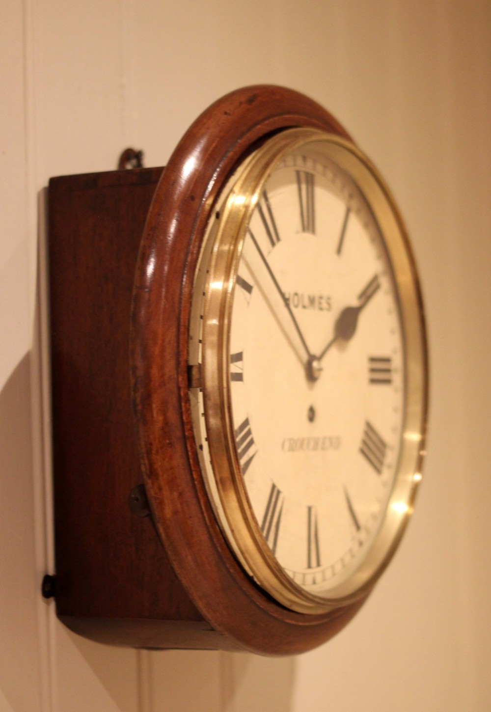 A circular mahogany wall clock featuring a brass bezel surrounding an off-white dial with black Roman numerals. View VII