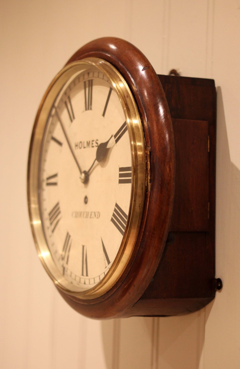 A circular mahogany wall clock featuring a brass bezel surrounding an off-white dial with black Roman numerals. View VIII