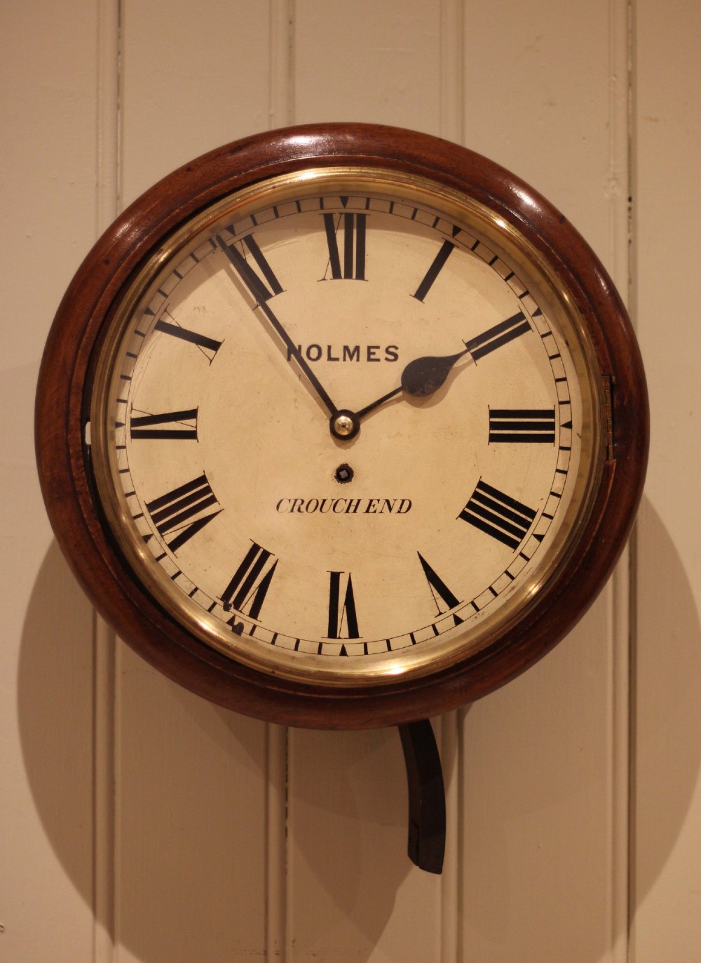 A circular mahogany wall clock featuring a brass bezel surrounding an off-white dial with black Roman numerals. View IX