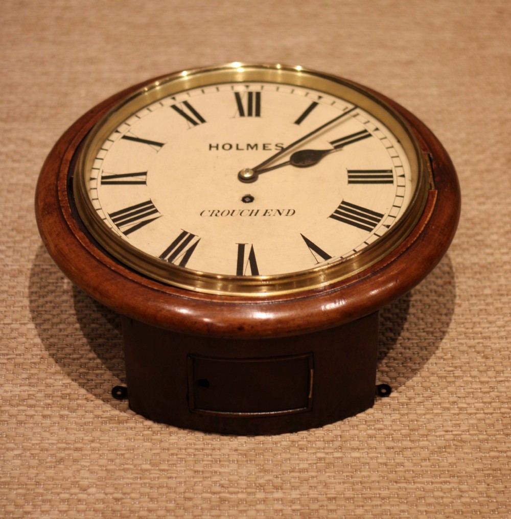 A circular mahogany wall clock featuring a brass bezel surrounding an off-white dial with black Roman numerals. View X