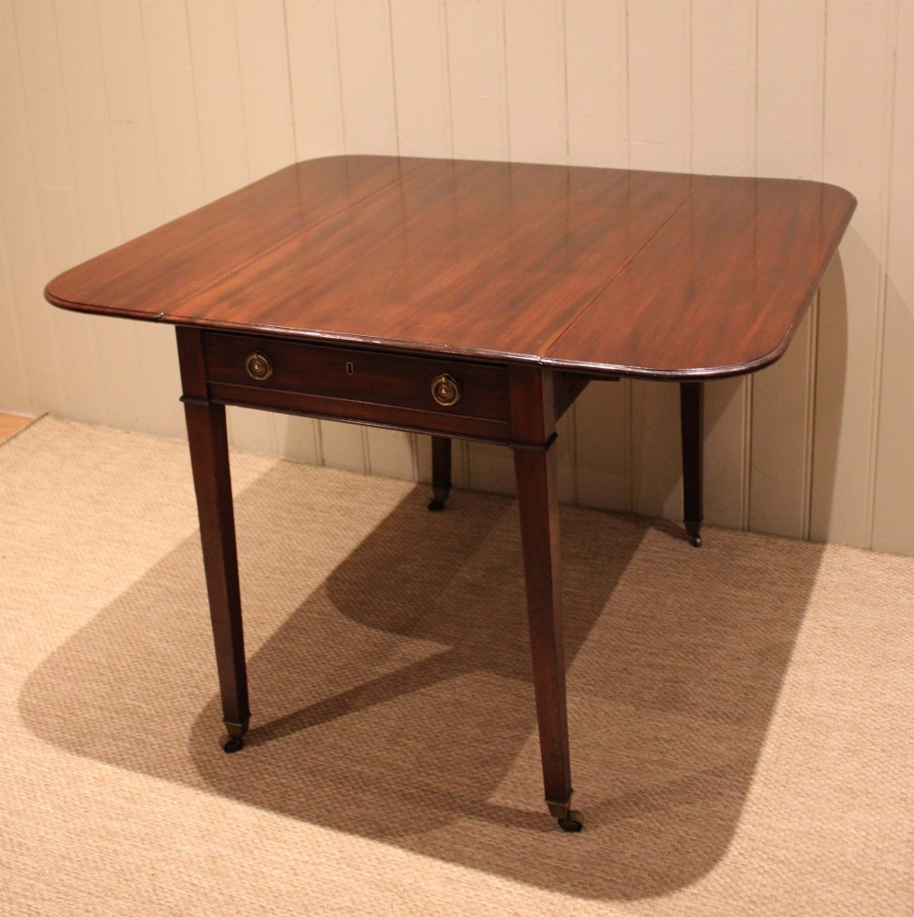 A solid mahogany Pembroke table featuring two drop leaves, a central drawer with brass ring handles, and square tapered legs fitted with brass castors. View VIII