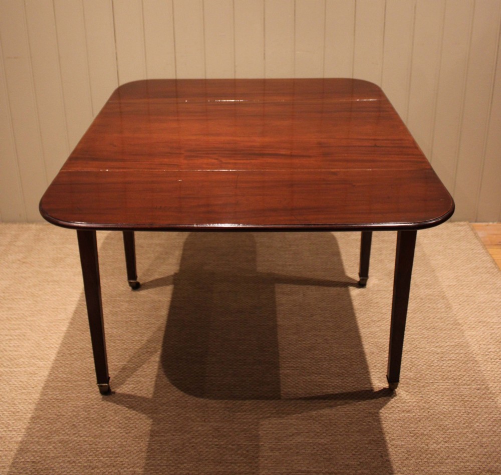 A solid mahogany Pembroke table featuring two drop leaves, a central drawer with brass ring handles, and square tapered legs fitted with brass castors. View XI
