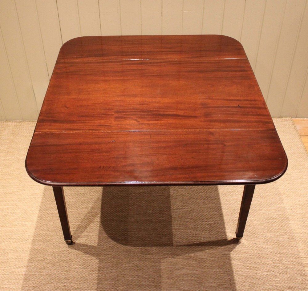 A solid mahogany Pembroke table featuring two drop leaves, a central drawer with brass ring handles, and square tapered legs fitted with brass castors. View XII