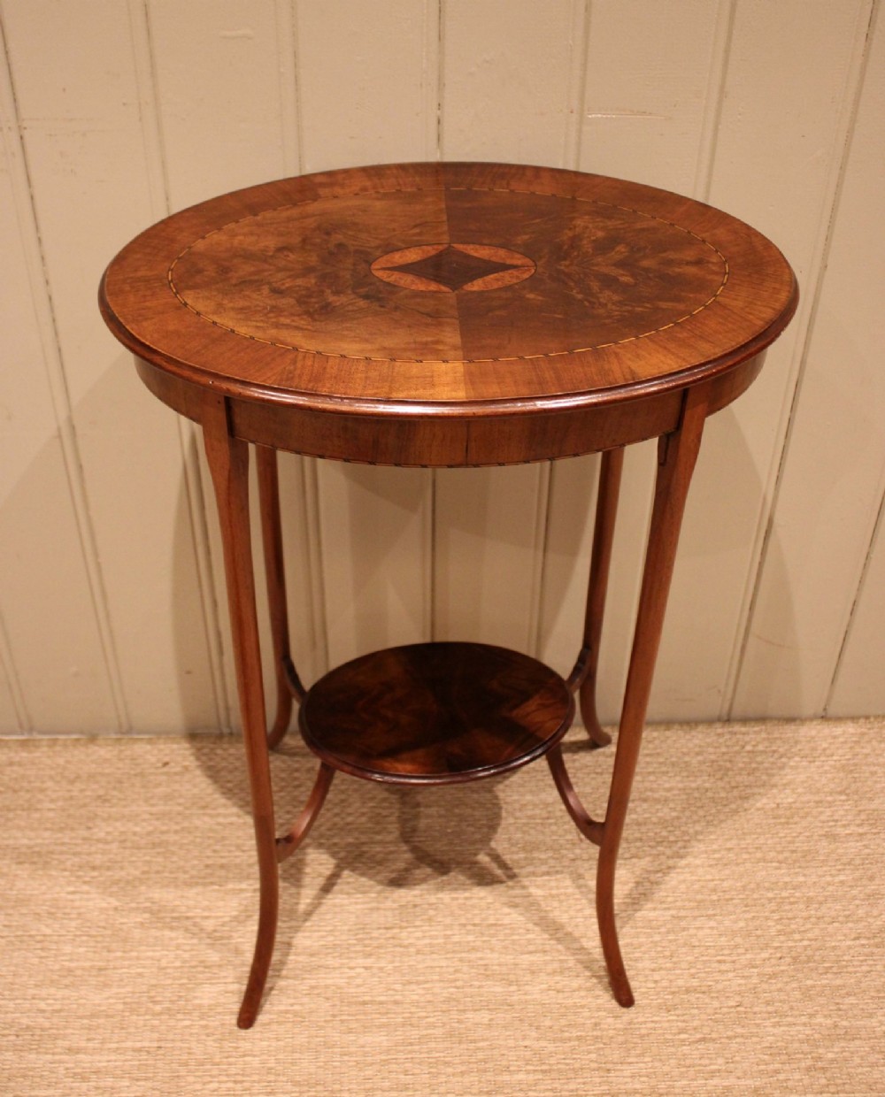 An Edwardian oval mahogany occasional table featuring crossbanded veneer inlay, a central geometric medallion motif, slender swept legs, and a small circular lower shelf.
