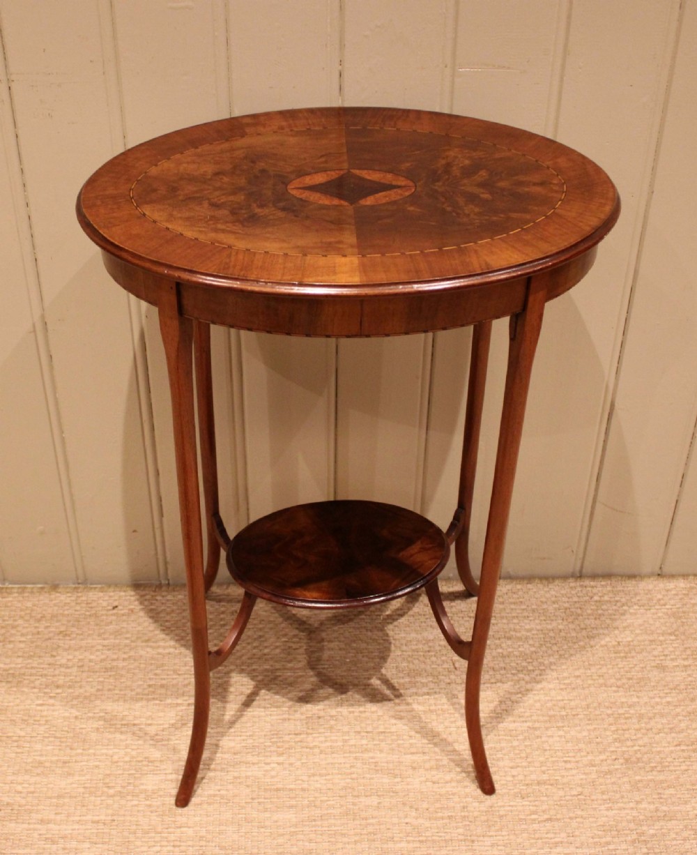 An Edwardian oval mahogany occasional table featuring crossbanded veneer inlay, a central geometric medallion motif, slender swept legs, and a small circular lower shelf. View II