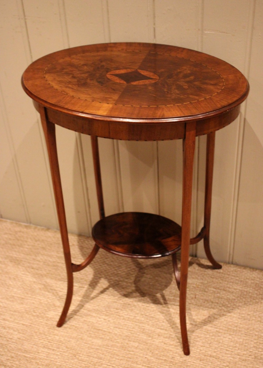 An Edwardian oval mahogany occasional table featuring crossbanded veneer inlay, a central geometric medallion motif, slender swept legs, and a small circular lower shelf. View IV