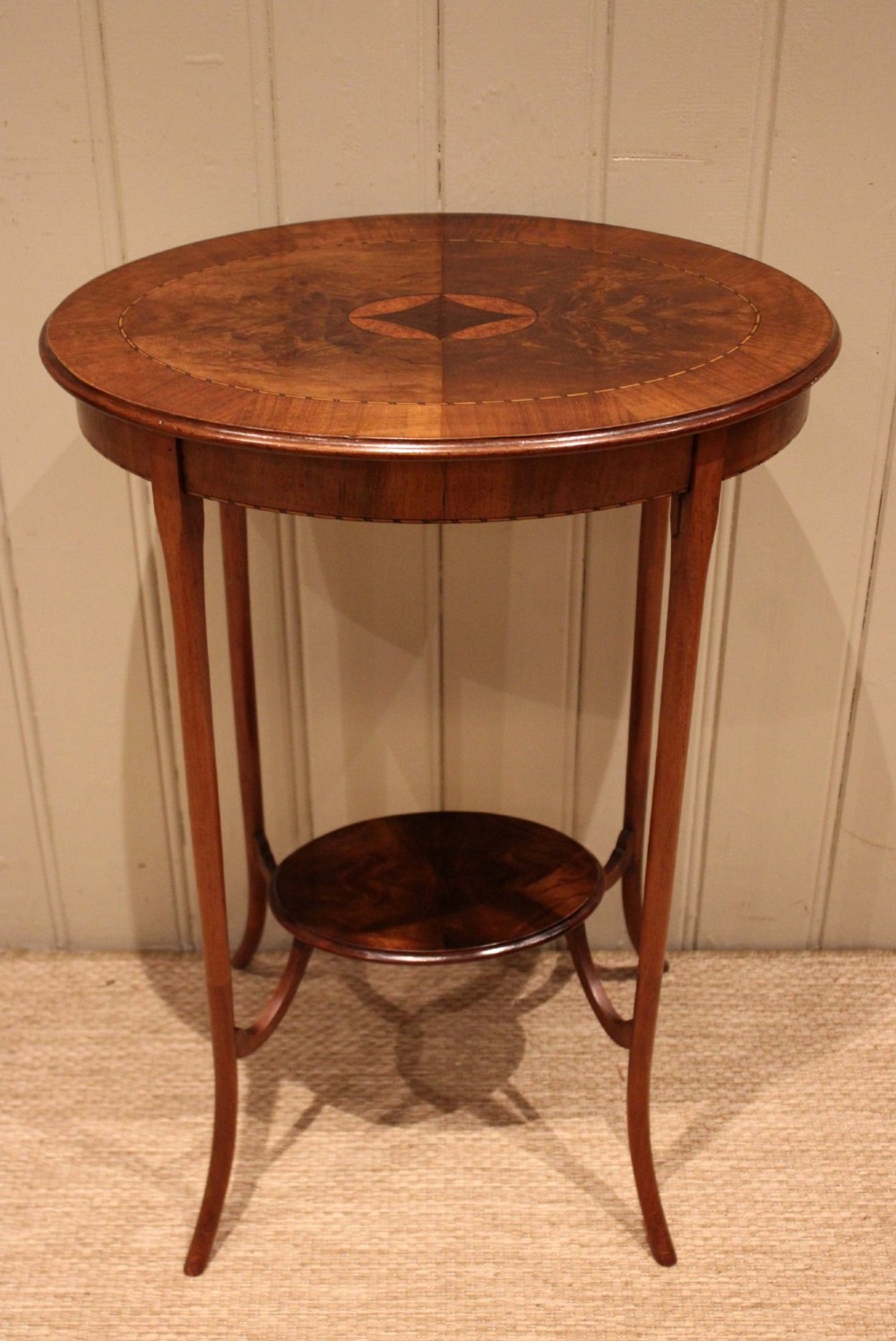An Edwardian oval mahogany occasional table featuring crossbanded veneer inlay, a central geometric medallion motif, slender swept legs, and a small circular lower shelf. View V