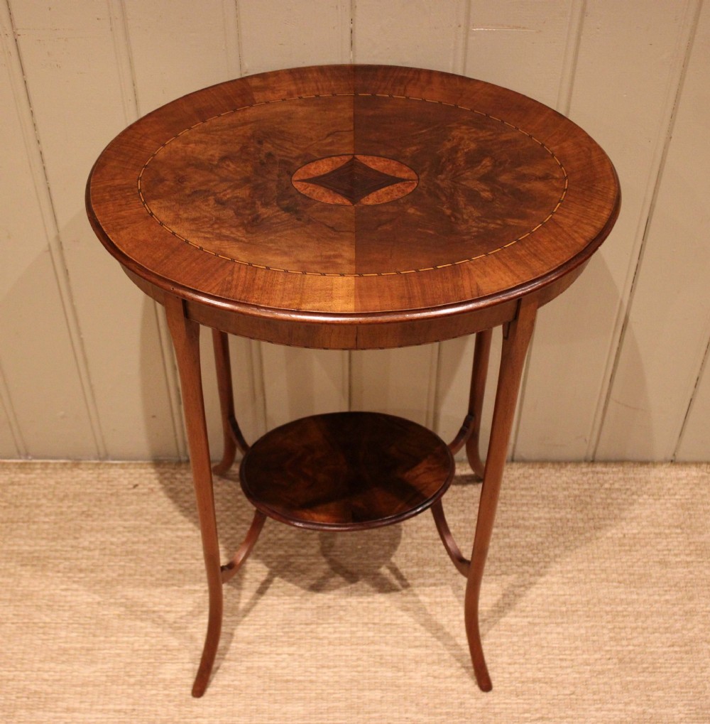 An Edwardian oval mahogany occasional table featuring crossbanded veneer inlay, a central geometric medallion motif, slender swept legs, and a small circular lower shelf. View VI