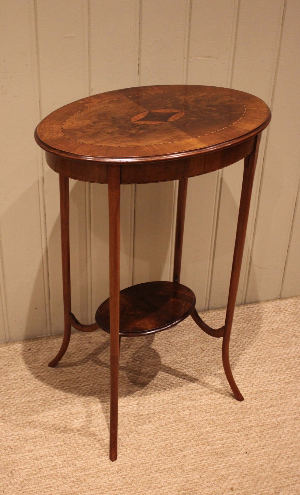 An Edwardian oval mahogany occasional table featuring crossbanded veneer inlay, a central geometric medallion motif, slender swept legs, and a small circular lower shelf. View VII