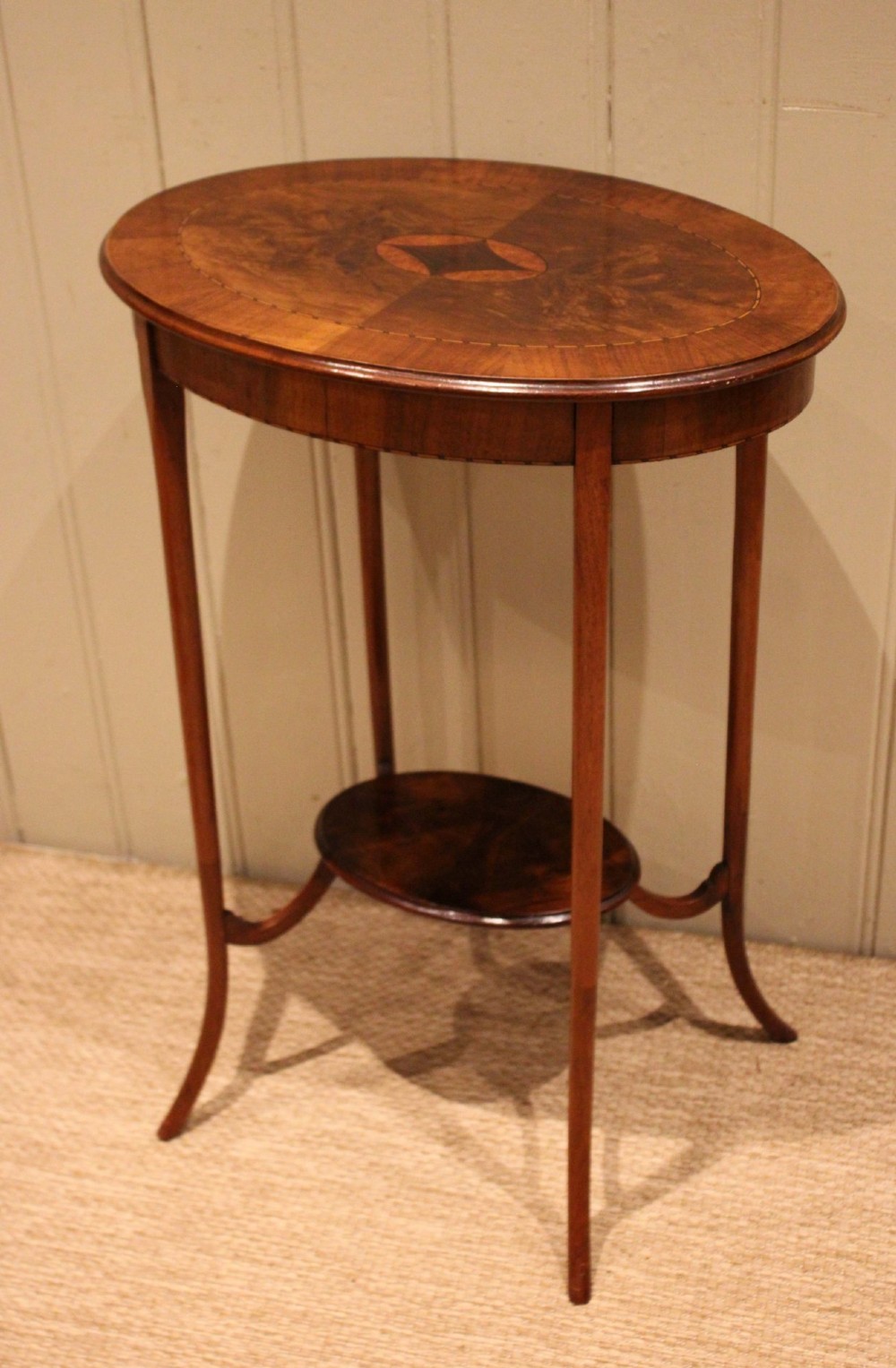 An Edwardian oval mahogany occasional table featuring crossbanded veneer inlay, a central geometric medallion motif, slender swept legs, and a small circular lower shelf. View VIII