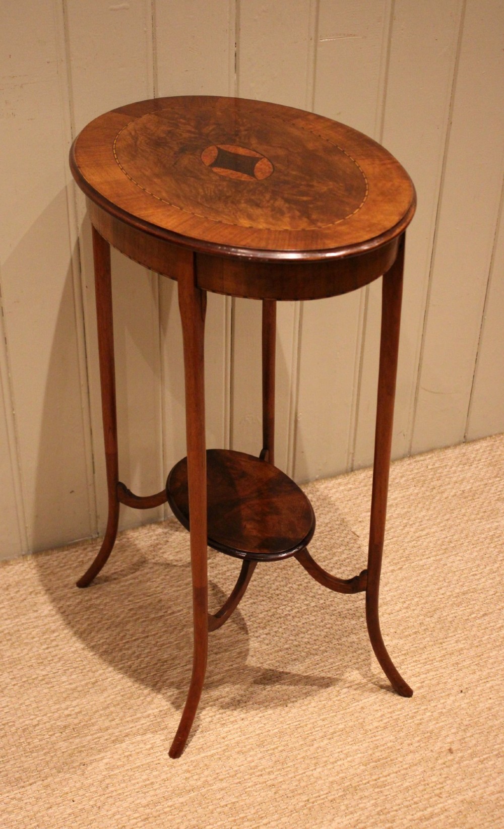 An Edwardian oval mahogany occasional table featuring crossbanded veneer inlay, a central geometric medallion motif, slender swept legs, and a small circular lower shelf. View X