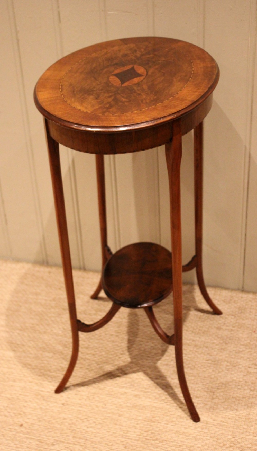 An Edwardian oval mahogany occasional table featuring crossbanded veneer inlay, a central geometric medallion motif, slender swept legs, and a small circular lower shelf. View XI